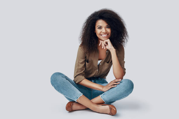 istock Beautiful young African woman smiling and looking at camera while sitting against grey background 1201182878