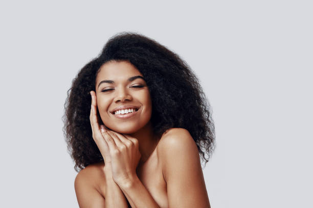 istock Beautiful young African woman keeping eyes closed and smiling while standing against grey background 1201183727