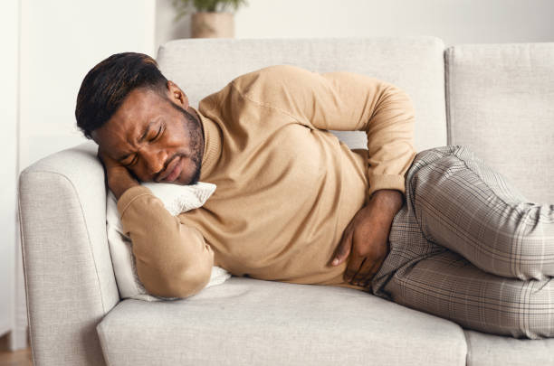 istock Afro Man Touching Aching Stomach Lying On Couch At Home 1201185598