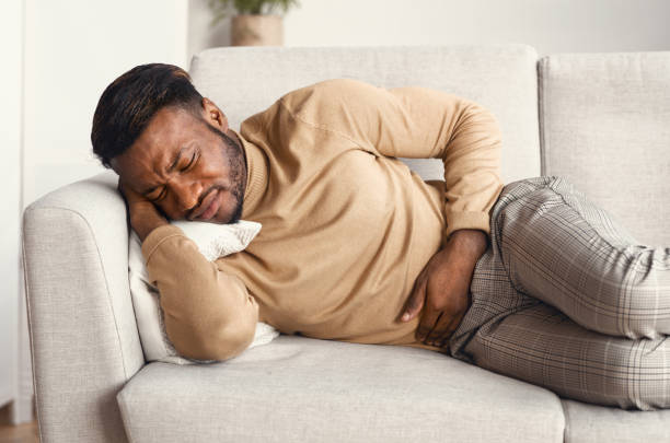 Afro Man Touching Aching Stomach Lying On Couch At Home Stomachache. Afro Man Suffering From Abdominal Pain Touching Aching Stomach Lying On Couch At Home food poisoning stock pictures, royalty-free photos & images