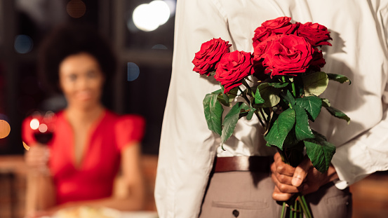 Romance In Relationship. Unrecognizable Afro Man Holding Bouquet Of Roses Having Romantic Date With Girfriend In Restaurant. Panorama, Selective Focus