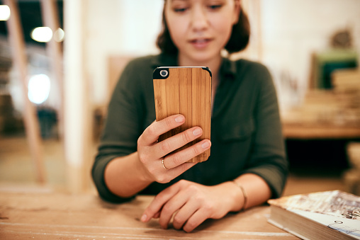 Cropped shot of a female carpenter using her cellphone while sitting in her workshop