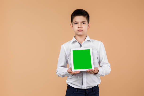 istock Little boy with tablet on light yellow studio background. 1201195765
