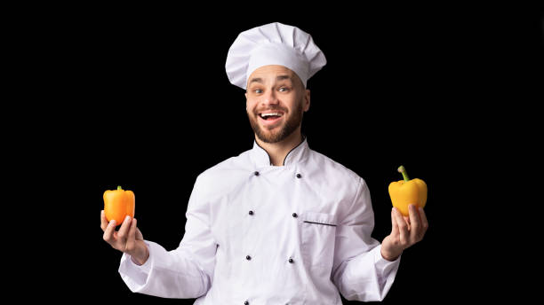 istock Chef Holding Two Yellow Sweet Peppers Posing, Black Background, Panorama 1201198236