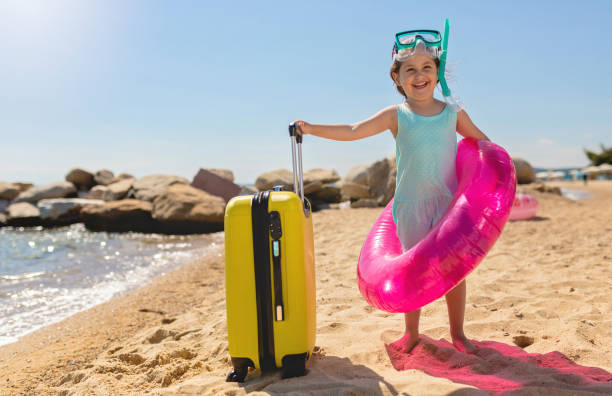 istock Happy 4 year old girl with suitcase on the beach 1201200928