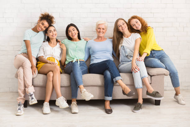 Women Of Different Age Sitting On Sofa Smiling Indoor Diverse Women Of Different Age Sitting On Sofa Smiling To Camera Indoor. Support Group Concept group of women all ages stock pictures, royalty-free photos & images