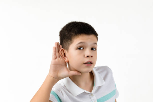 happy little child boy in striped t-shirt making hearing gesture on white background. facial expression. kid with hand over ear listening gossip.