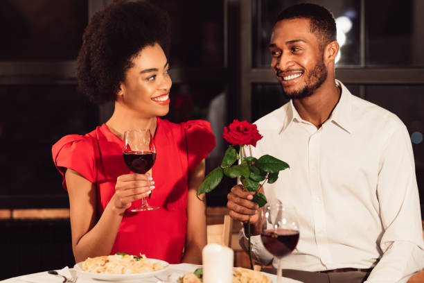 homme donnant la rose à la femme ayant la date de valentine dans le restaurant - anniversary couple rose black photos et images de collection