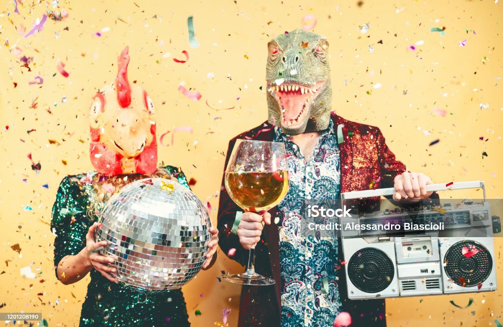 Crazy couple celebrating new year eve wearing chicken and dinosaur t-rex mask - Young trendy people having fun drinking champagne and listening music with vintage boombox - Absurd and holidays concept Party - Social Event Stock Photo