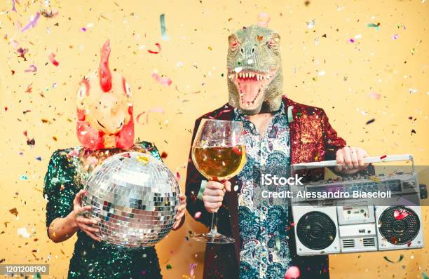 Crazy Couple Celebrating New Year Eve Wearing Chicken And Dinosaur Trex Mask Young Trendy People Having Fun Drinking Champagne And Listening Music With Vintage Boombox Absurd And Holidays Concept Stock Photo - Download Image Now
