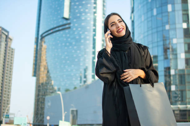 Happy Arabic woman with shopping bag talking on mobile phone on the street Happy Arabic woman with shopping bag talking on mobile phone on the street emirati culture photos stock pictures, royalty-free photos & images