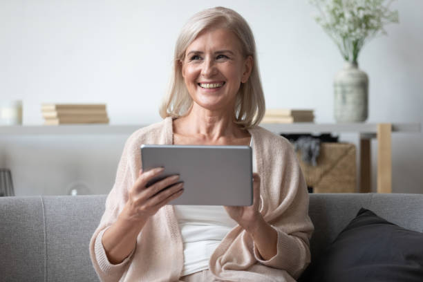 istock Happy senior woman smiling using tablet at home 1201208578