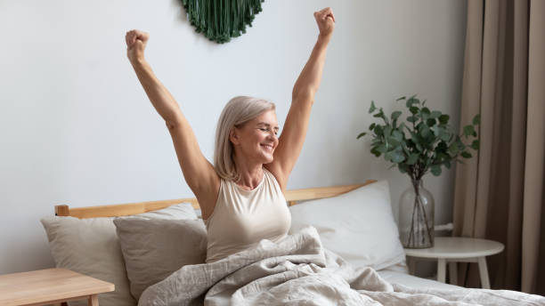 mujer anciana sonriente estirando en la cama dando la bienvenida a un nuevo día - despertar fotografías e imágenes de stock