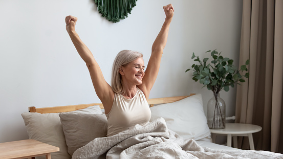 Smiling elderly woman stretching in bed welcoming new day