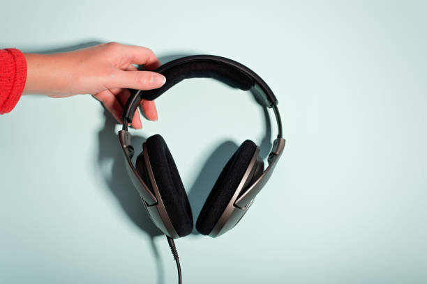 istock Black massive headphones in female hand on pastel background, copy space. Modern technology flat lay with over-ear earphones in woman hand, modern lifestyle concept 1201209790