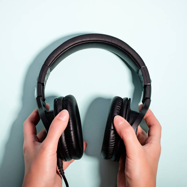 istock Black massive headphones in female hand on pastel background, copy space. Modern technology flat lay with over-ear earphones in woman hand, modern lifestyle concept 1201209792