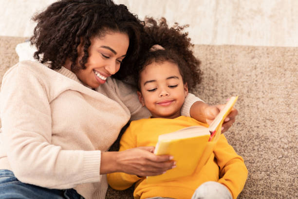 istock Mother And Daughter Reading Book Sitting On Sofa At Home 1201214773