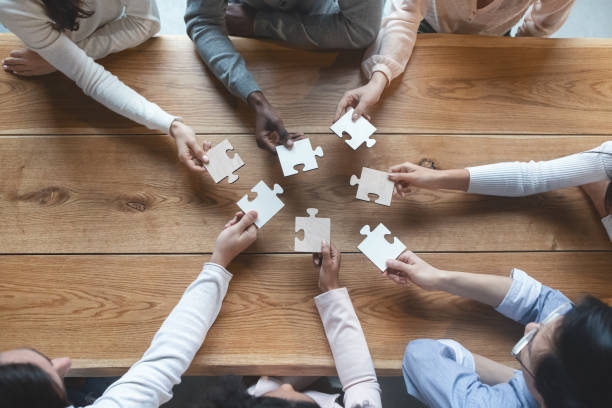Creative team sitting at table and putting together puzzle pieces Startup and teamwork concept, top view of creative multiracial team sitting at table and putting together puzzle pieces jigsaw piece photos stock pictures, royalty-free photos & images