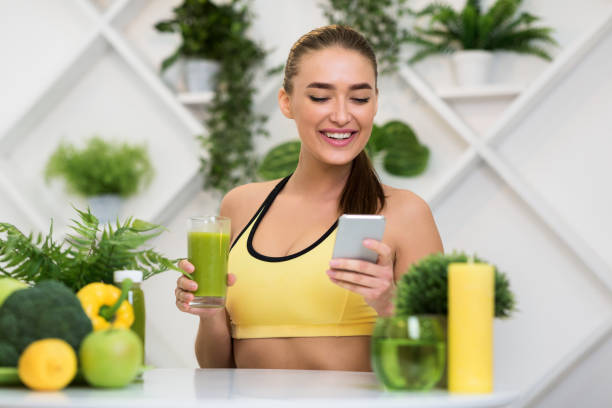 istock Happy woman using phone and drinking green smoothie juice 1201215767
