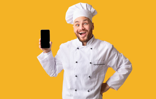 istock Excited Chef Showing Mobile Phone Empty Screen On Yellow Background 1201216547