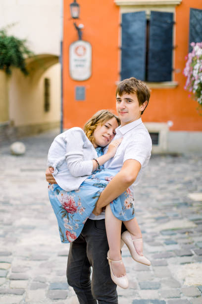 istock smiling young handsome man holding on hands his happy disabled girlfriend, while standing outdoors, on the background of old orange building 1201216791