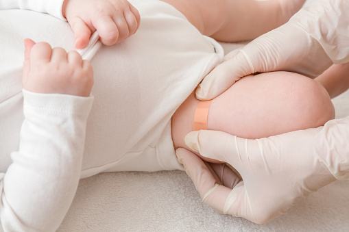 Manos de doctor en guantes protectores de goma blanca poniendo vendaje adhesivo en la pierna del bebé después de la inyección de la vacuna. Concepto médico. Closeup. photo