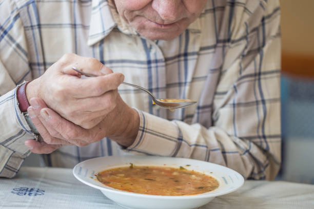 l'homme âgé avec la maladie de parkinson retient la cuillère dans les deux mains. - grelotter photos et images de collection