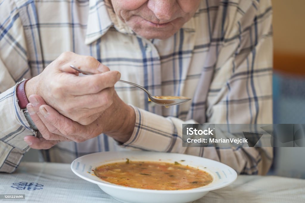 Elderly man with Parkinsons disease holds spoon in both hands. Parkinson's Disease Stock Photo