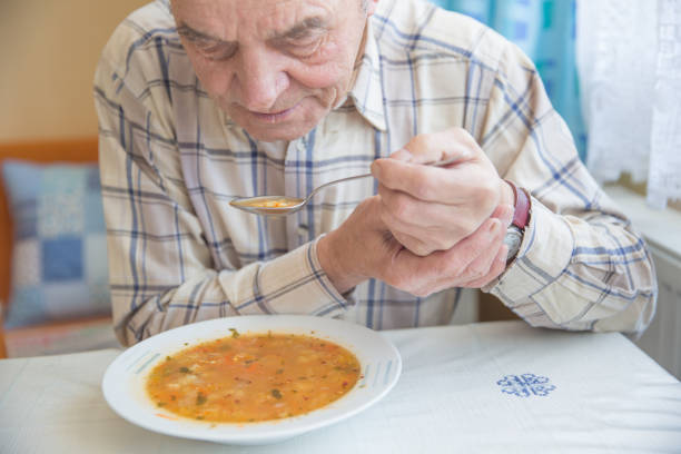 istock Elderly man with Parkinsons disease holds spoon in both hands. 1201221505