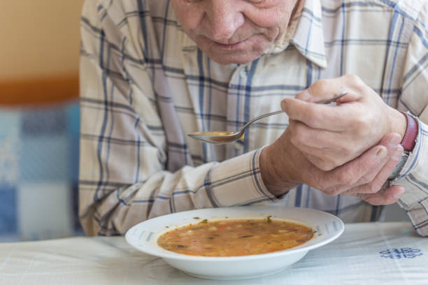 istock Elderly man with Parkinsons disease holds spoon in both hands. 1201221543