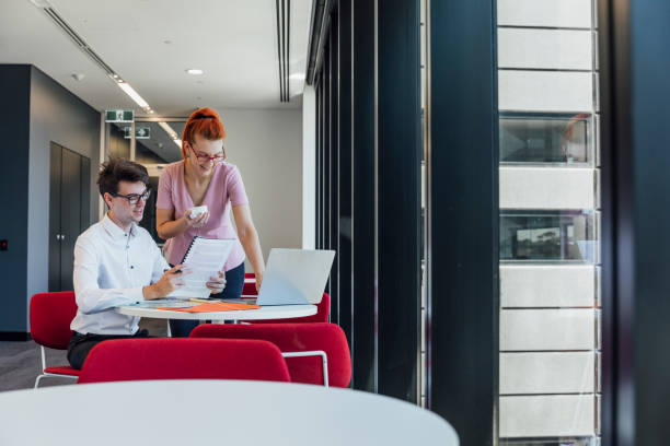 Her Input is Invaluable Young man and woman sitting at a table working together with a laptop open in front of them. They are smiling two heads are better than one stock pictures, royalty-free photos & images