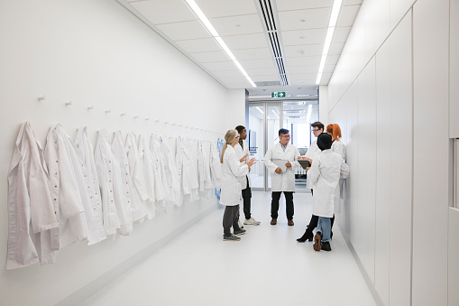 Medical protective clothing hanging in a hallway. A team of medical scientist gather around talking