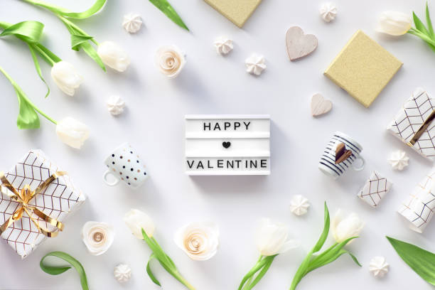 istock Valentines day flat lay, top view on white background with fresh tulip flowers, coffee cups, gift wrapped in geometric paper with golden lines and marshmallows. Text 