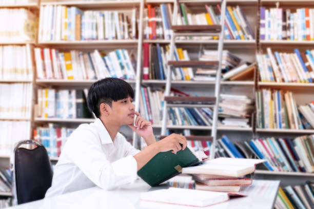 istock Young teenager reading and ,searching data from book,at library,blurry light around 1201238039