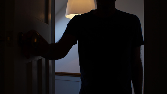Silhouette of a man opening a door to a dark room.