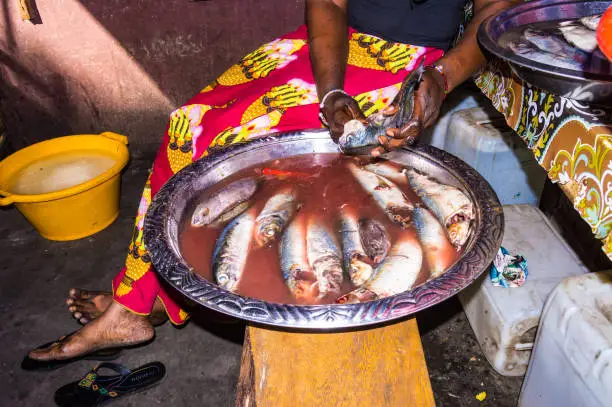 Gambian woman uses her hands to empty and clean fish for meal preparation on a Banjul market.
