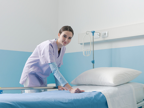 Expert smiling nurse working at the hospital, she is making the bed and changing sheets, healthcare and medicine concept