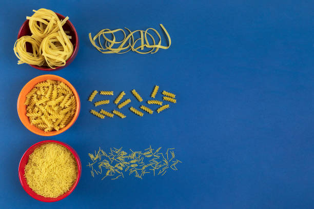 row of multicolored bowls with different types of pasta on classic blue background. ingredients for cooking, food concept. top view with copy space - pasta directly above fusilli food imagens e fotografias de stock