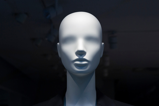 A close-up of a mannequin's head in a window of a mall on the dark background with switched off electric lamps on the ceiling. Copy space.