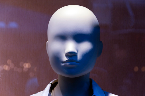 A close-up of a mannequin's head in a shop window with pink fabric and blurred lights in the background.