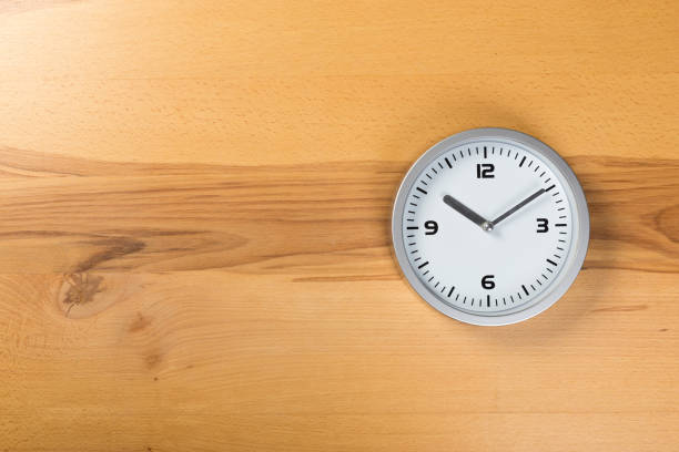 istock minimalist white wall clock with light metal on wooden background texture 1201263487