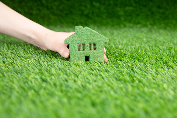 A man holds in his hand a small eco house. A miniature copy of a house on the grass. stock photo