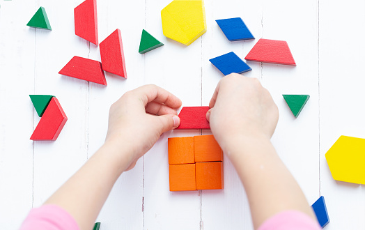 Un niño juega con bloques de colores construye un modelo sobre un fondo de madera clara. Casa photo