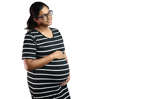A pregnant lady wearing spectacles with black dress with white stripes and hands on belly looking up in delight with copy space for text.
