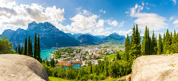 Aerial panoramic view at the popular touristic landmark Riva del Garda village at lake Garda, Italy. on a beautiful summer day. Blue water, rocks, mountains, sunlight and clear sky.