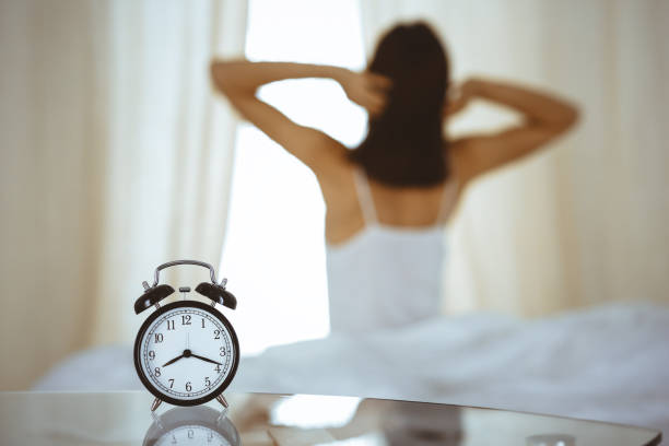 Woman stretching hands in bed after wake up, sun flare . Brunette entering a day happy and relaxed after good night sleep and back view. Concept of a new day and joyful weekend Woman stretching hands in bed after wake up, sun flare . Brunette entering a day happy and relaxed after good night sleep and back view. Concept of a new day and joyful weekend. smash alarm clock stock pictures, royalty-free photos & images