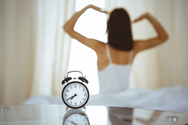 Woman stretching hands in bed after wake up, sun flare . Brunette entering a day happy and relaxed after good night sleep and back view. Concept of a new day and joyful weekend Woman stretching hands in bed after wake up, sun flare . Brunette entering a day happy and relaxed after good night sleep and back view. Concept of a new day and joyful weekend. smash alarm clock stock pictures, royalty-free photos & images