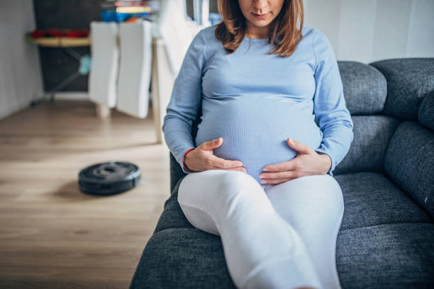 istock Pregnant woman resting while robot vacuum cleaner cleaning floor 1201285451