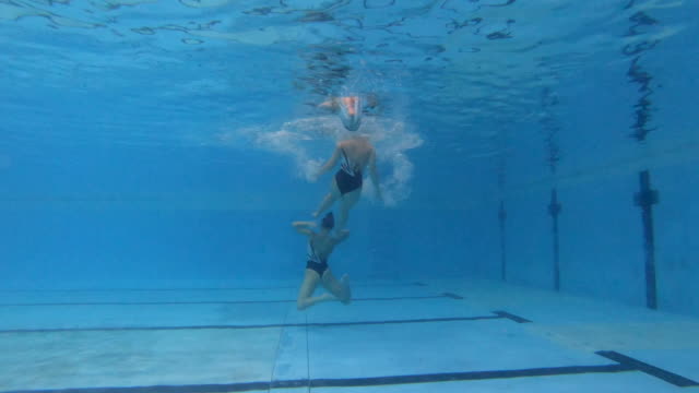 Underwater video of a woman jumping out of the water during a synchronized swimming choreography