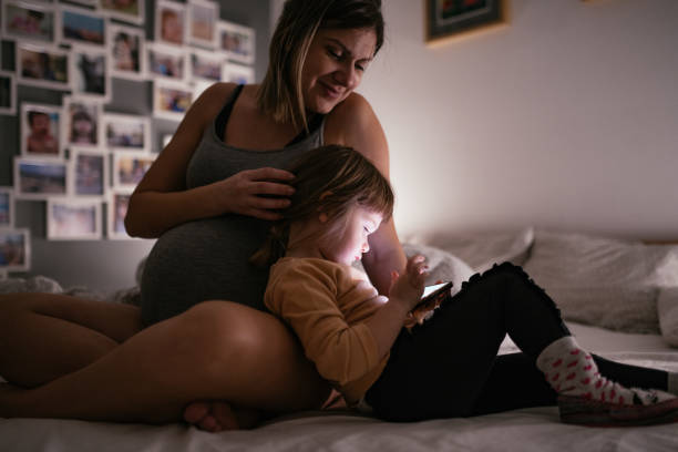 istock Mother cuddles young girl who is using mobile phone for gaming 1201287304